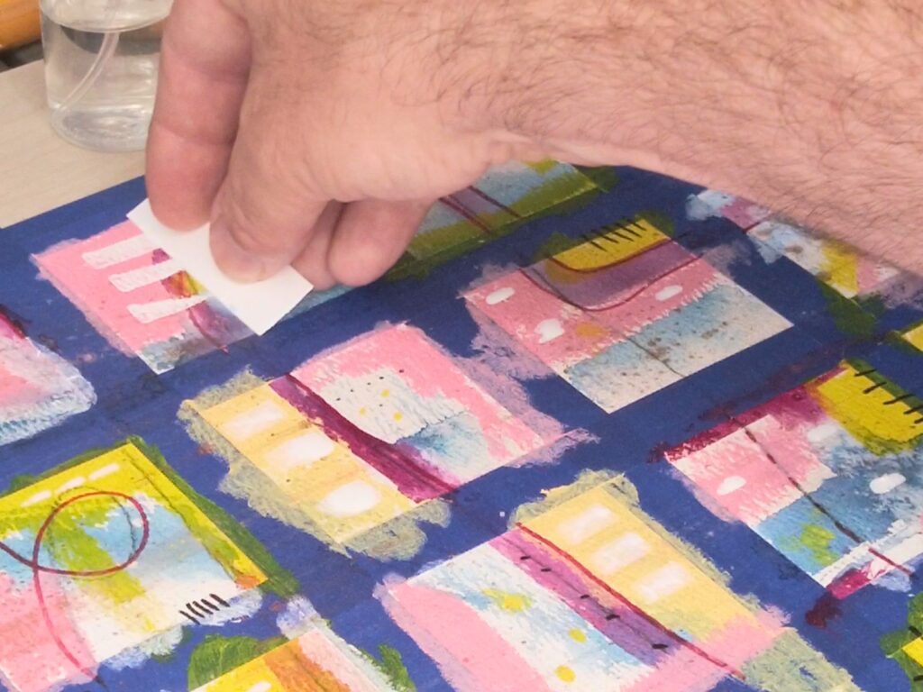 Kevin working across the gridded artwork with paint and mark-making materials spread around the work surface.